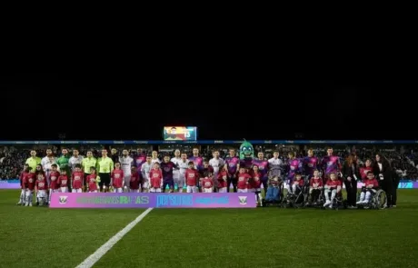 Die Spieler zweier Fußballmannschaften posieren mit Kindern, einige im Rollstuhl, hinter einem Banner zur Sensibilisierung für seltene Krankheiten.