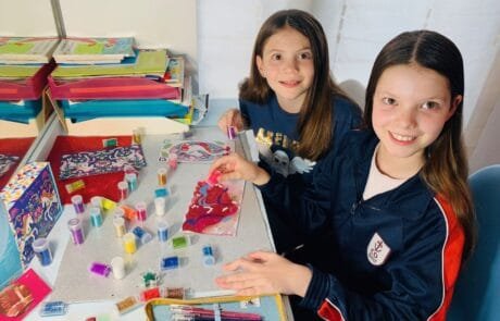 Carolina und eine Mitschülerin verzieren in der Schule Einhorn-Zeichnungen mit Glitzer.