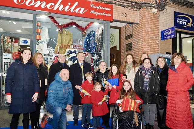 Gruppenfoto vor dem Geschäft Conchita, mit mehreren Kindern in rotem Mantel und einem Mädchen im Rollstuhl im Vordergrund.