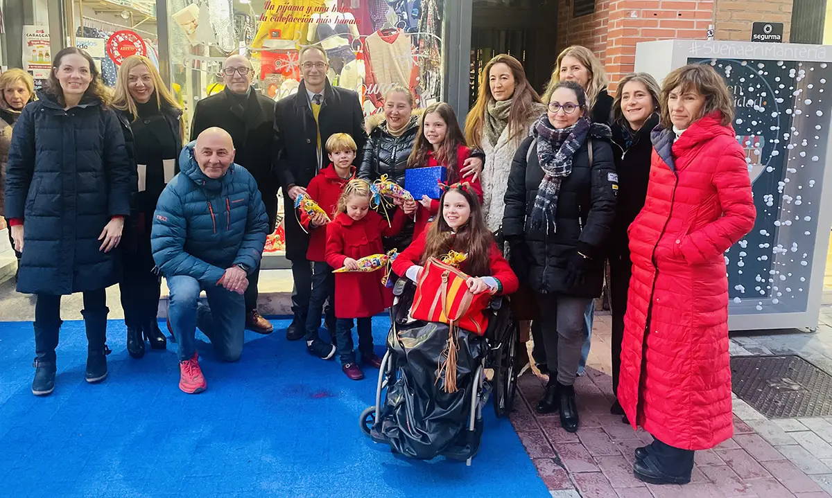 Gruppenfoto vor einem weihnachtlich geschmückten Geschäft in der Calle Mantería, mit einem Mädchen im Rollstuhl in der Mitte.