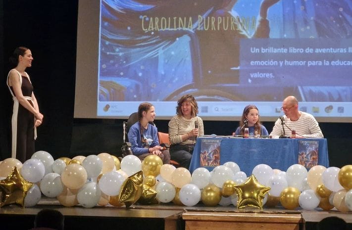 Podiumsgespräch auf der Bühne einer Schule: vier Personen am Tisch, eine am Mikrofon, zwischen goldenen und weißen Luftballons.