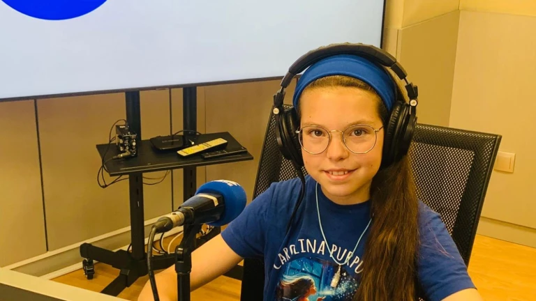 Isabel lächelt mit Kopfhörern und T-Shirt von „Carolina Purpurina“ vor dem Mikrofon eines Radiostudios.