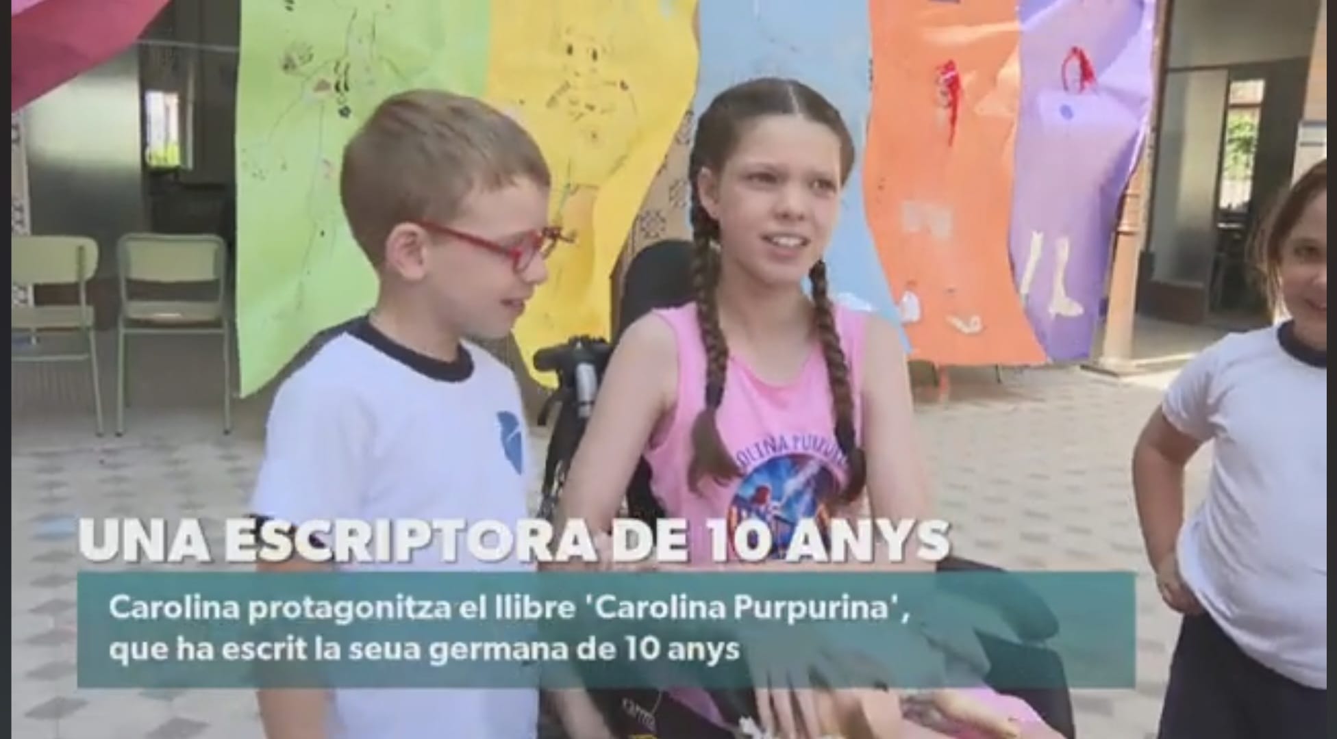Standbild aus der Nachrichtensendung von À Punt: Carolina unterhält sich im T-Shirt des Buches mit einem Jungen auf dem Schulhof.