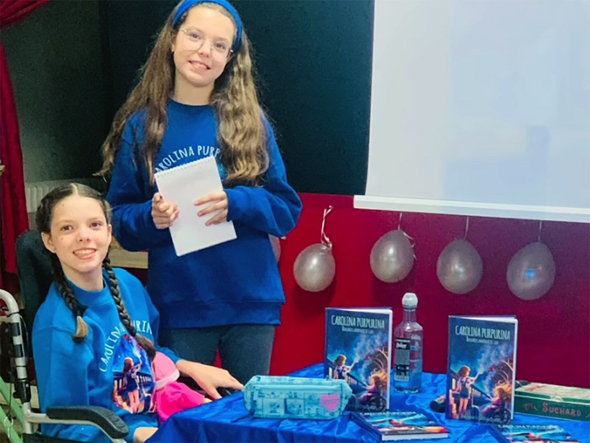 Isabel und Carolina neben dem Büchertisch während der Begegnung in der CEIP Marqués de Valero in Béjar.