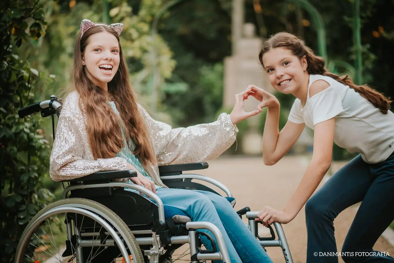 Carolina und Isabel formen in einem Park ein Herz mit den Händen.
