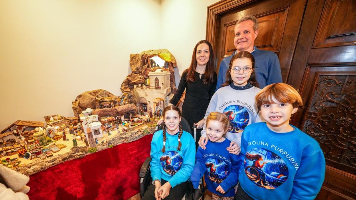 Zwei Erwachsene und vier Kinder in Carolina-Purpurina-Pullovern neben der Krippe; vorne Carolina in ihrem Rollstuhl.
