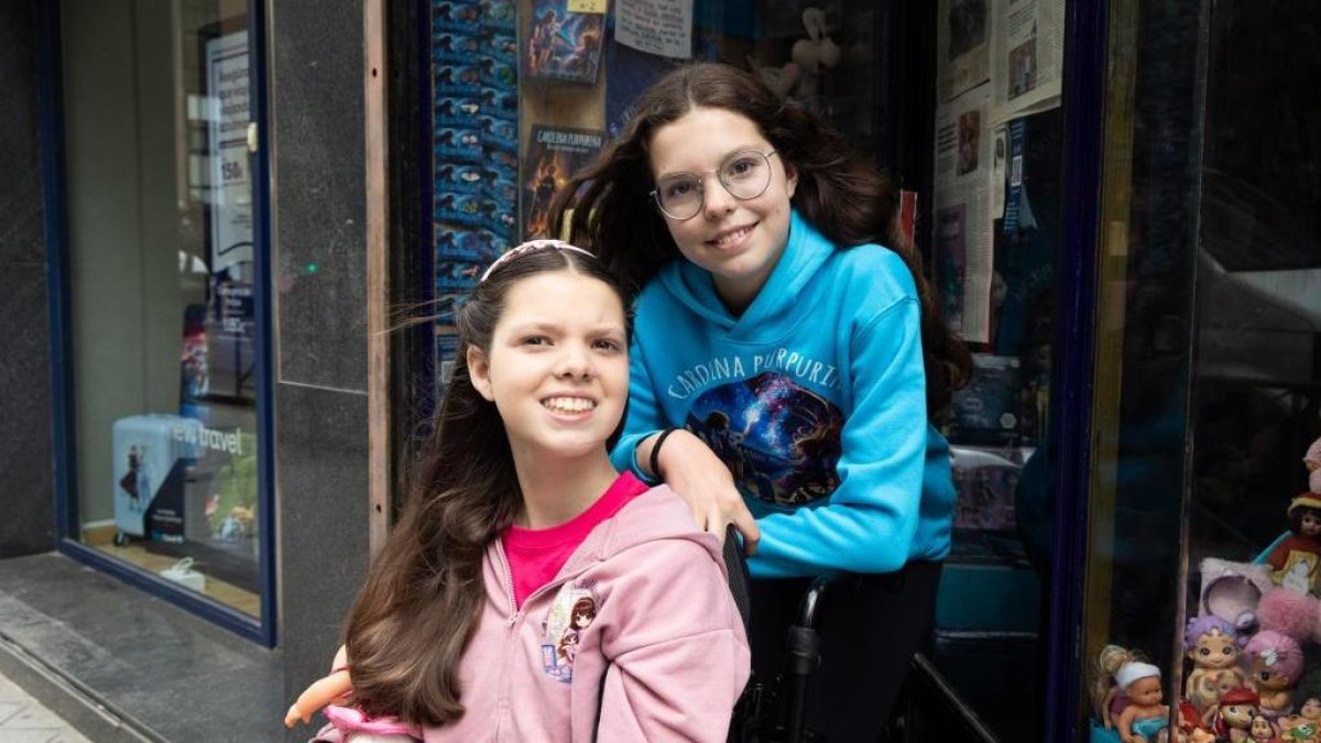 Carolina im Rollstuhl und Isabel im Carolina-Purpurina-Pulli posieren vor einem Schaufenster, in dem die Bücher der Reihe ausliegen.