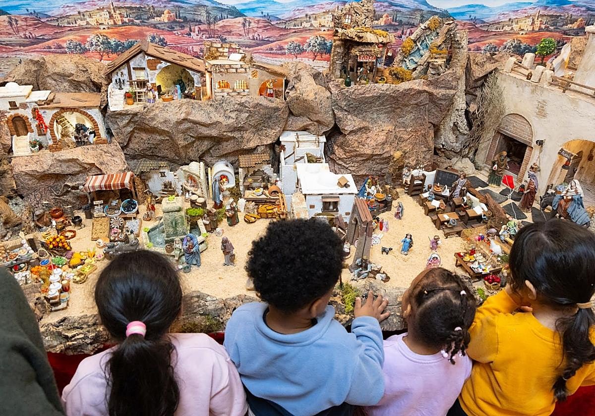 Erste Besucher der Krippe: Vier Kinder, von hinten gesehen, beugen sich über ihre Landschaft aus Felsen, Häusern und Figuren.